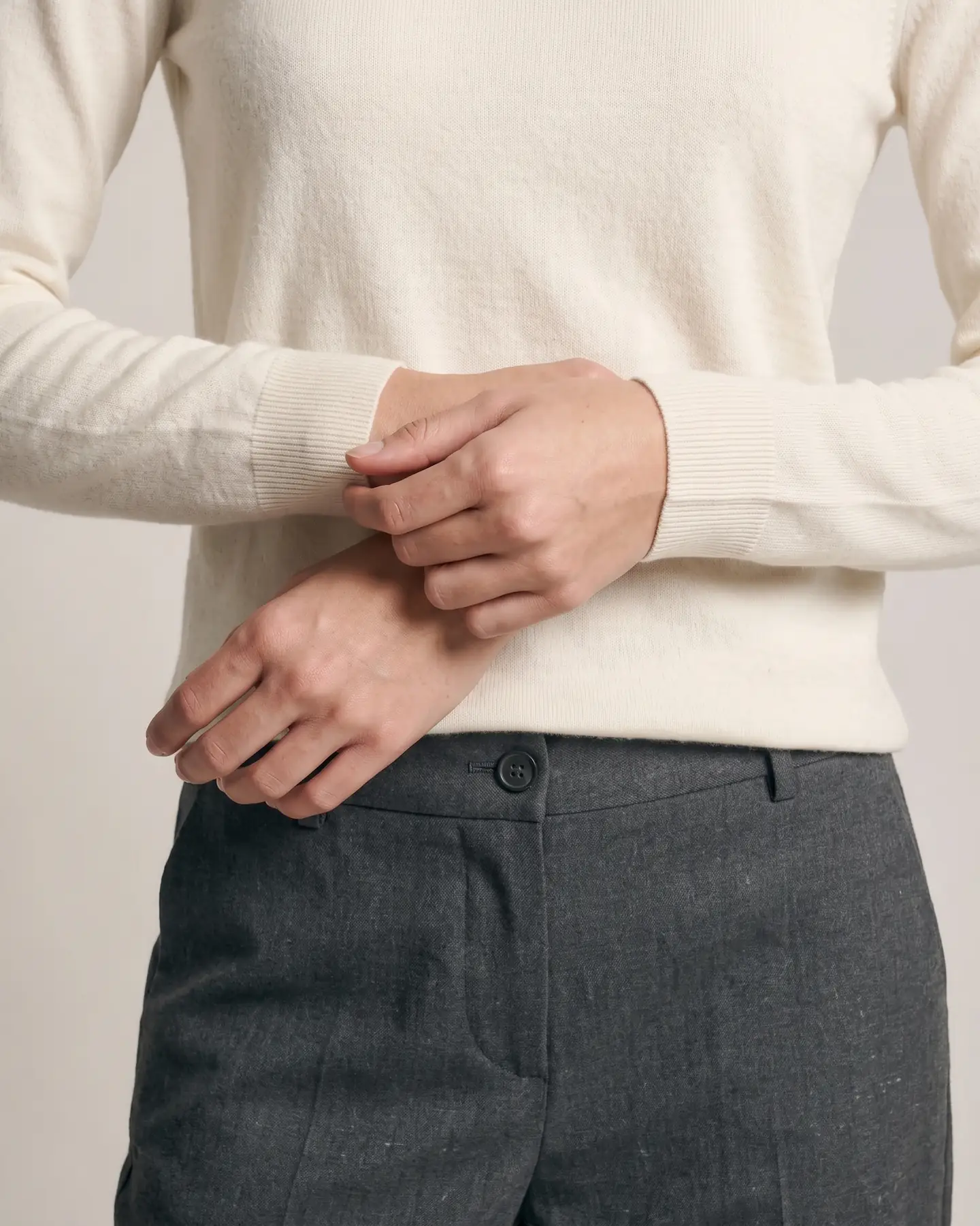 The hands at rest, the cuff rib reading against the grey wool